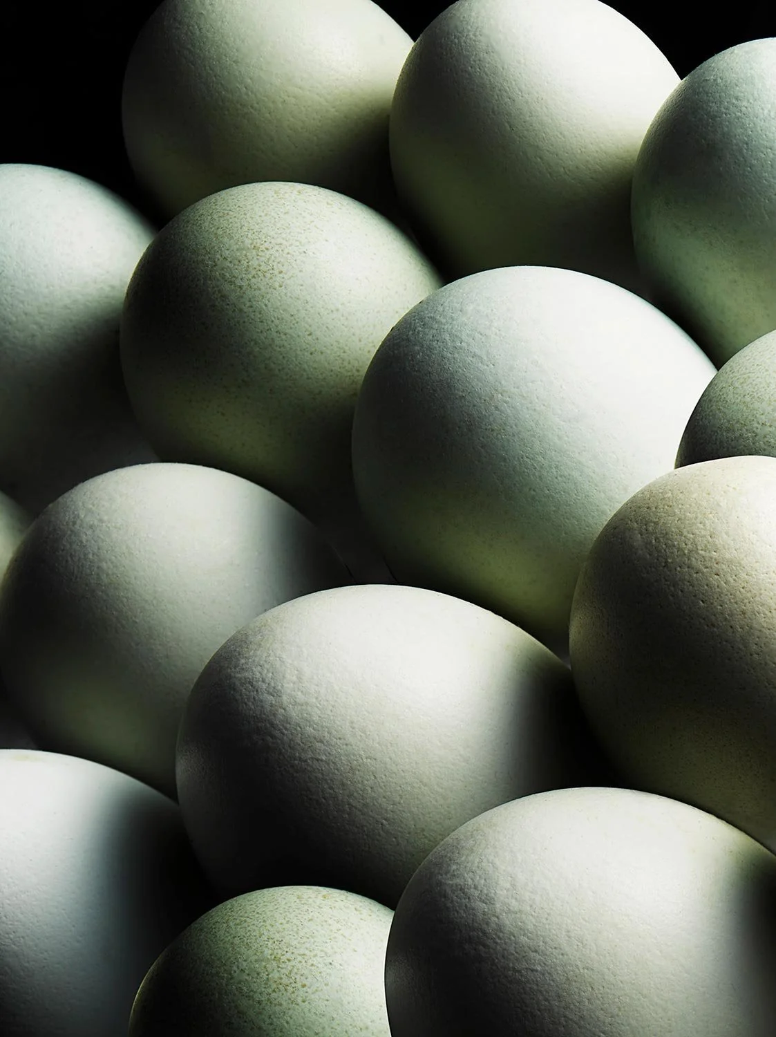 A close-up of multiple eggs with a smooth, matte surface, varying slightly in shades of white and light green, arranged in a dense cluster.