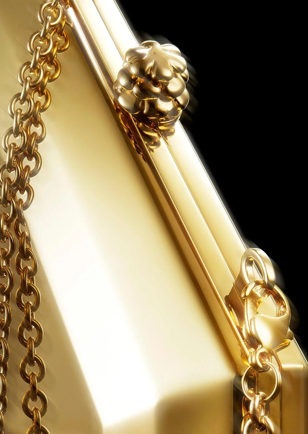 Close-up of a gold clutch bag with a decorative gold flower clasp and a gold chain strap.