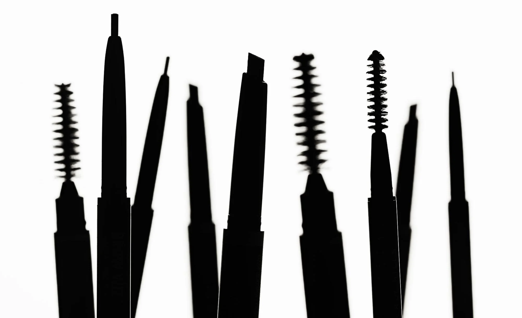 Silhouette of various makeup brushes and applicators against a white background.