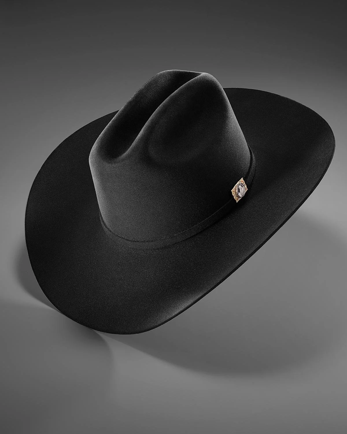 A black cowboy hat with a decorative band featuring a gemstone, placed against a plain grey background.