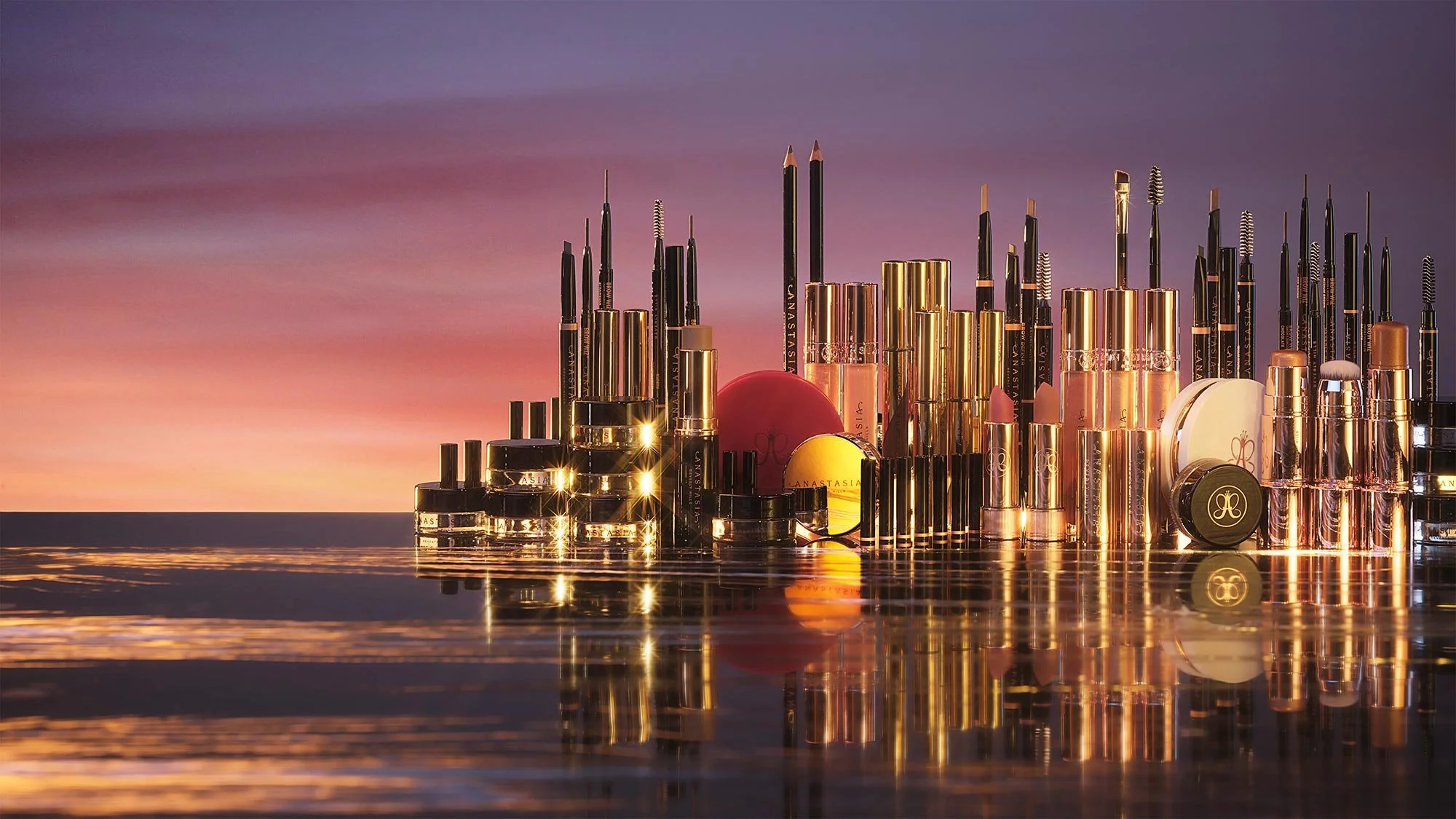 An array of makeup products, including lipsticks, lip glosses, and brushes, arranged on a reflective surface against a sunset sky background.