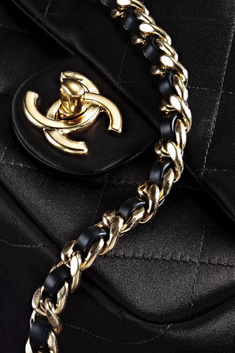 Close-up of a black quilted leather handbag featuring a gold turn-lock closure and a gold chain strap intertwined with black leather.