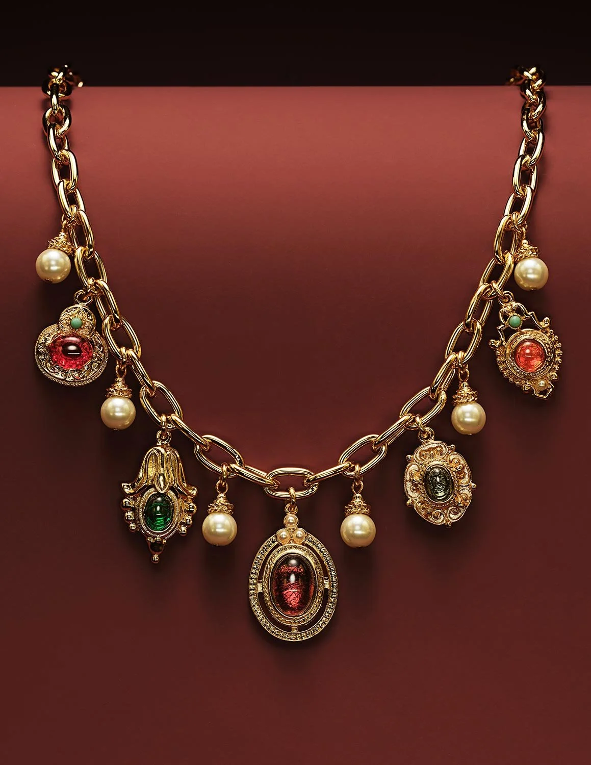 Gold chain necklace with charms and pearls displayed on a pink bust mannequin.