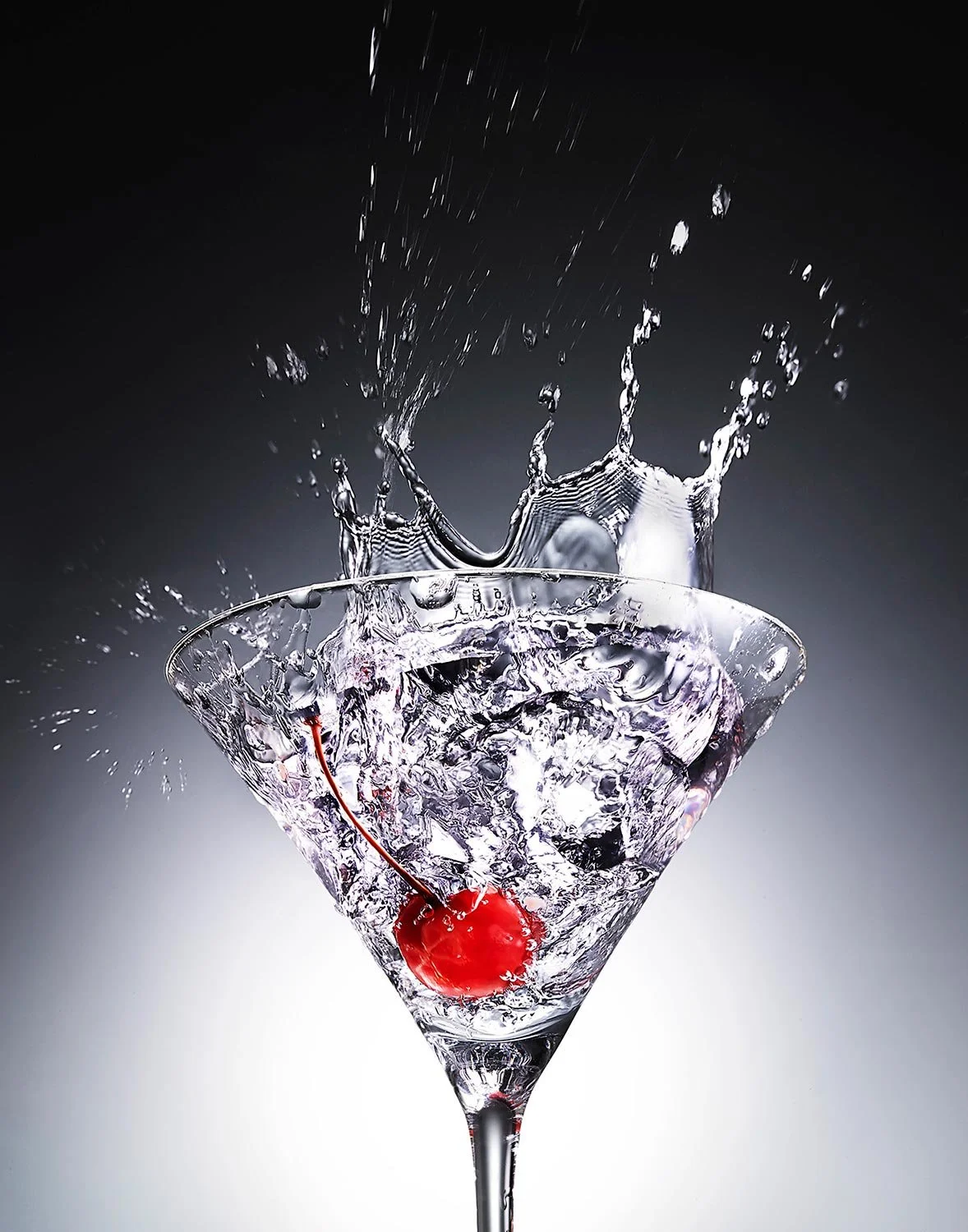 A cherry falling into a martini glass filled with water, creating splashes.