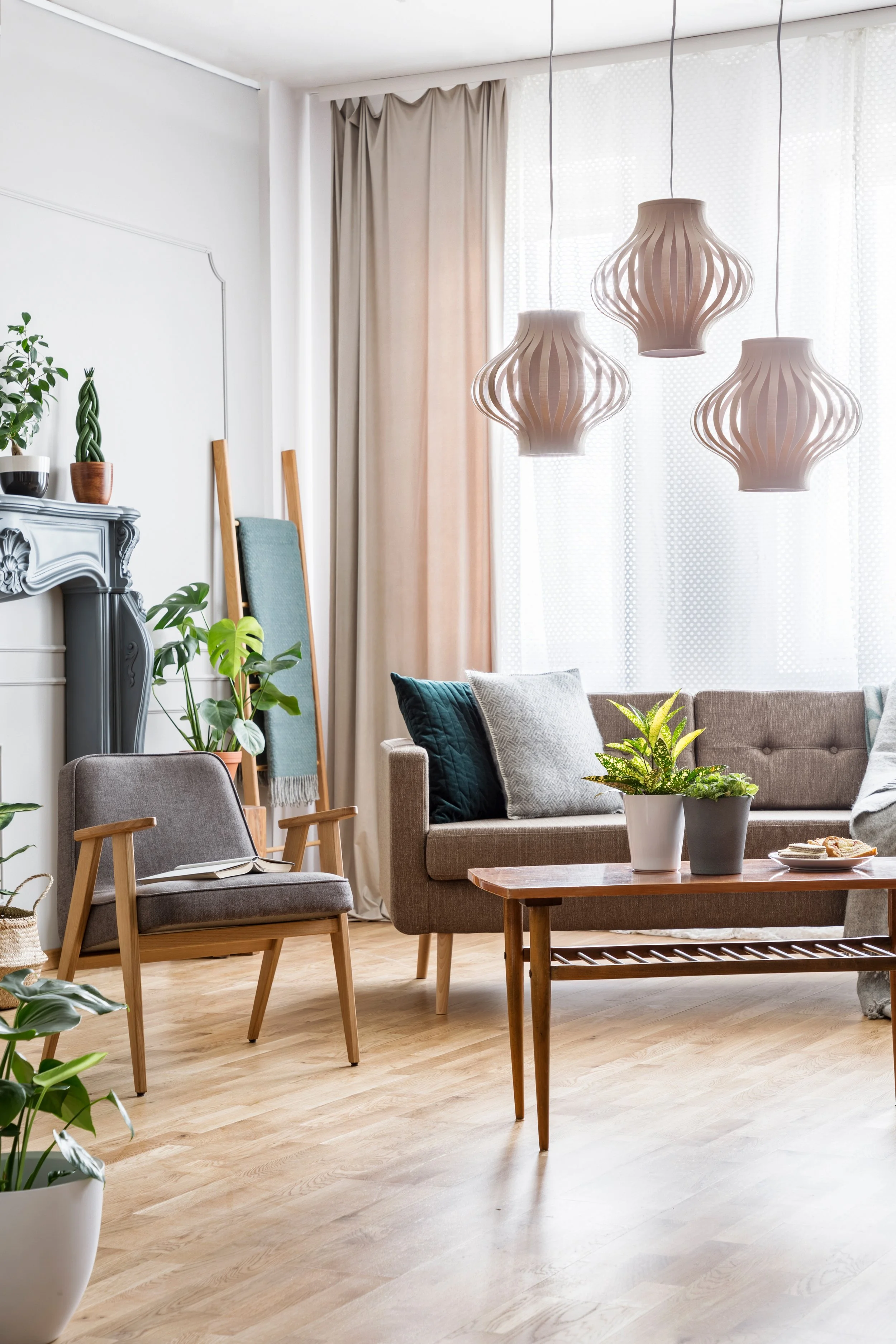 Brightly lit room with giant loft windows, grey couch and chair, potted plants on table and floor