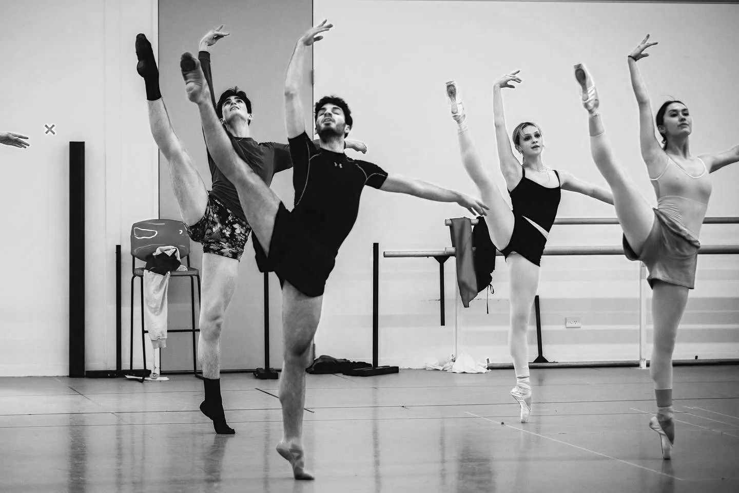 Ballet dancers practicing in a dance studio, lifting their legs high while balancing on pointe shoes.