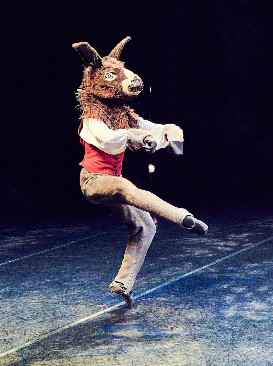 Person in a detailed animal costume, possibly a fennec fox or similar, dancing on stage with a dark background.