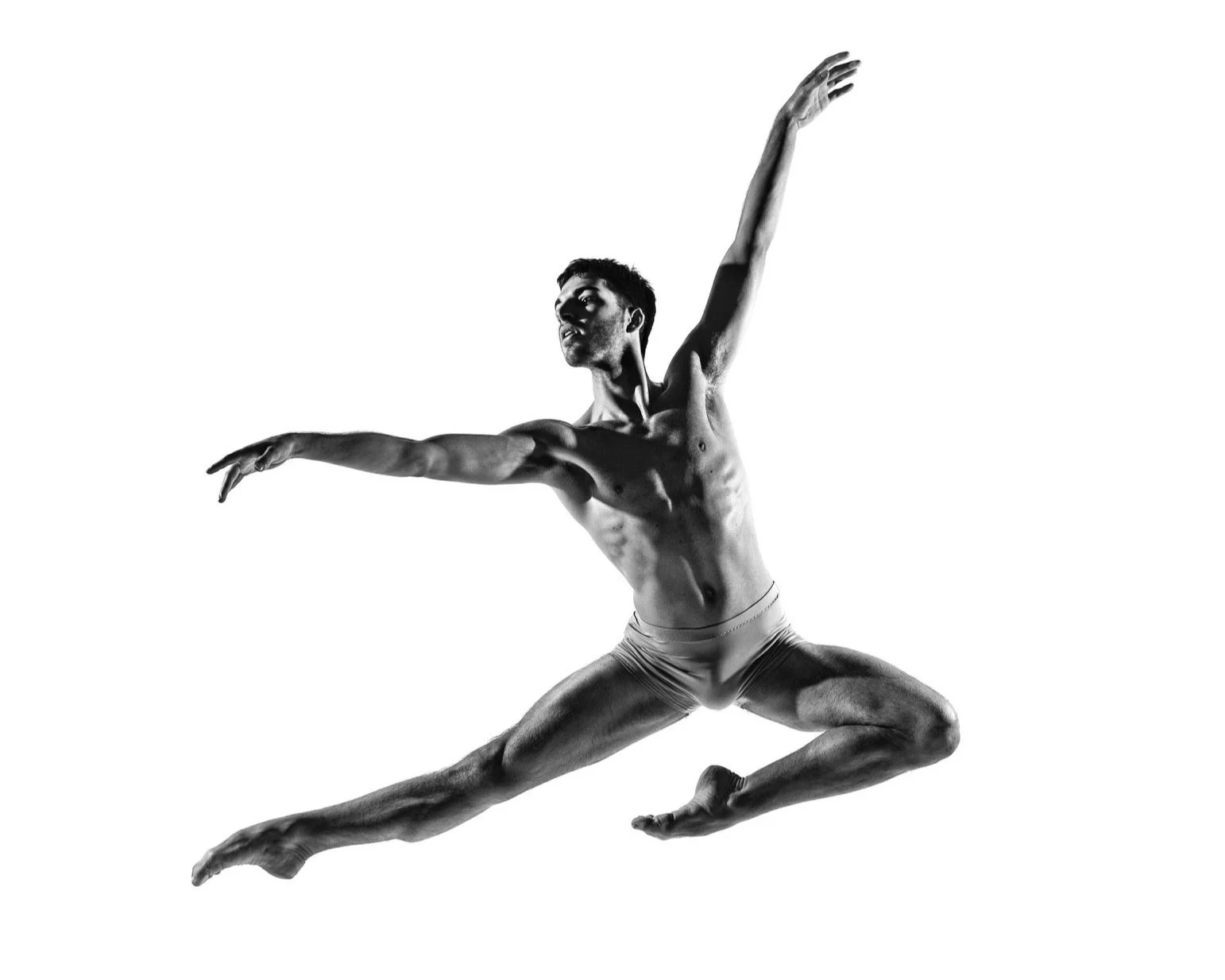 Black and white photo of a male ballet dancer mid-air, arms extended, legs spread wide in a jump, wearing only shorts.