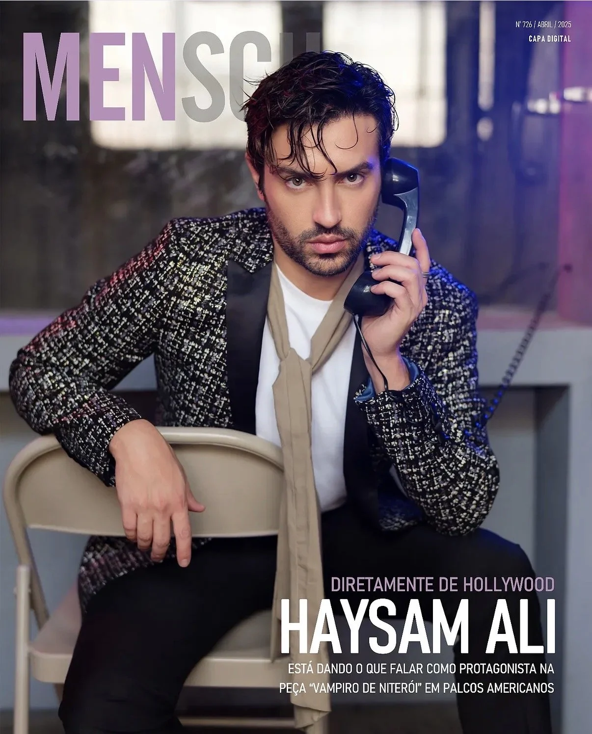 Magazine cover featuring Haysam Ali with dark hair and beard, wearing a patterned blazer, white shirt, and beige tie, holding a vintage telephone receiver to his ear, seated on a beige chair in an industrial setting with a blurred background.