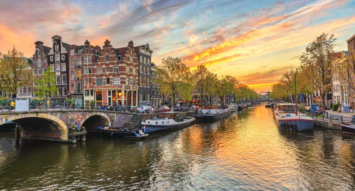 Ein malerischer Blick auf die Grachten bei Sonnenuntergang mit Booten am Wasser und historischen Gebäuden entlang der Grachten in Amsterdam.