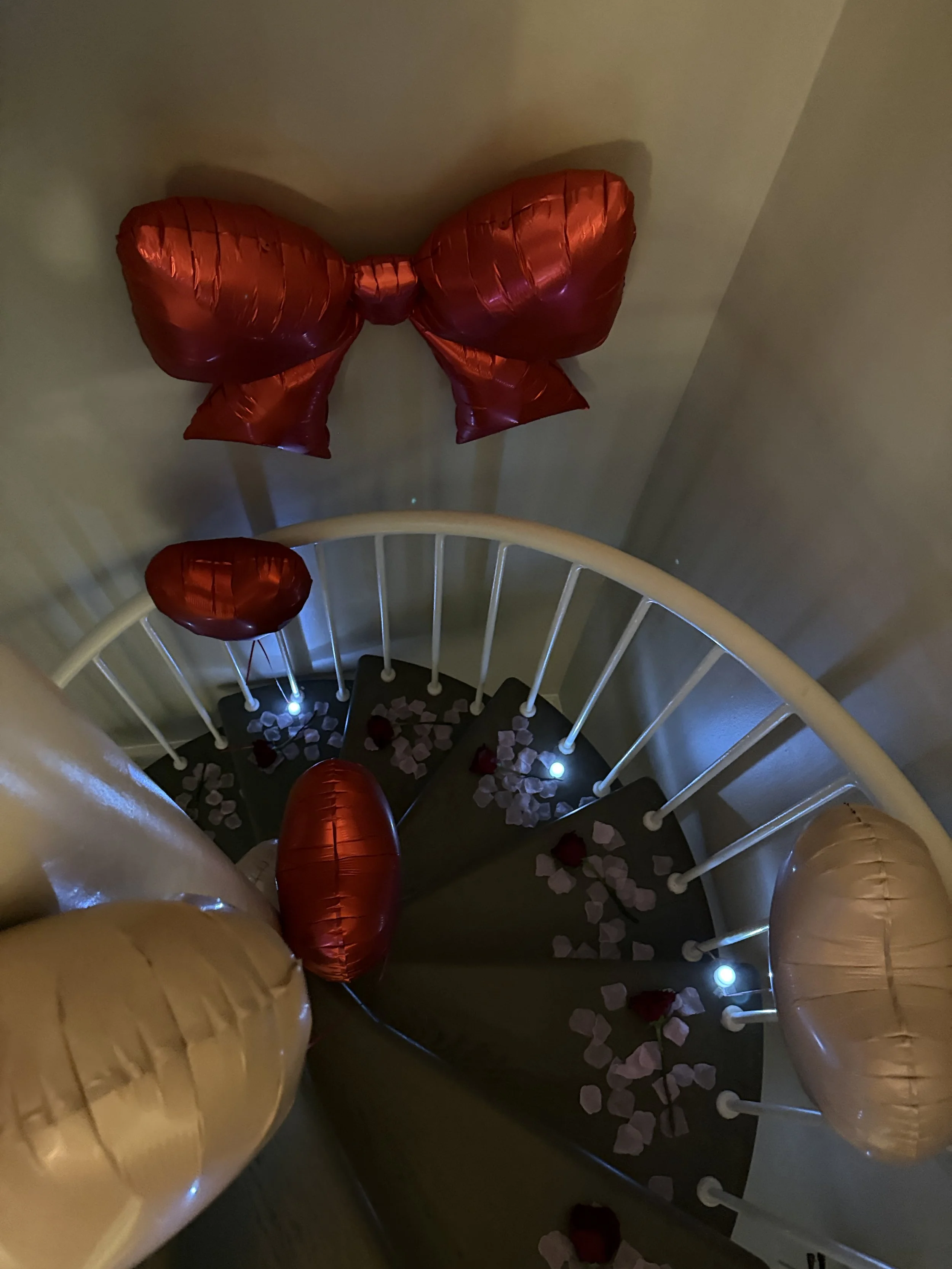 Stairway with rose petal trail and red roses on each step, romantic candles and balloons