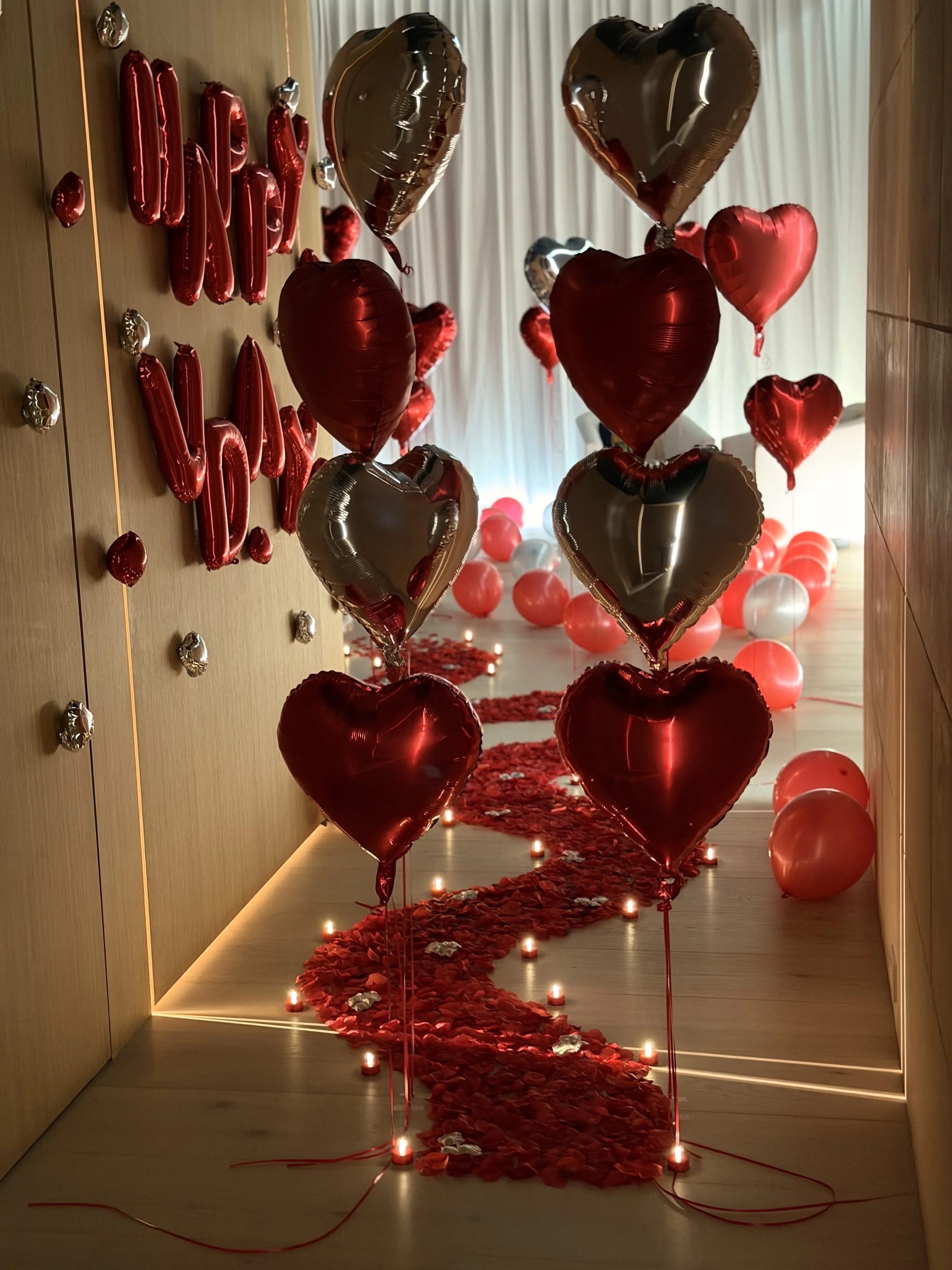 Luxury romantic room setup featuring a red rose petal path, balloons and ambient lighting.
