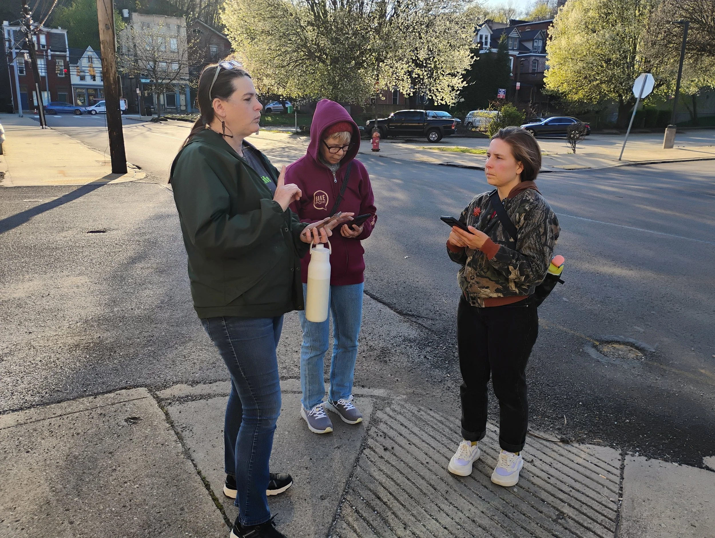 Three volulnteers standing at a sidewalk corner, using phones to collect survey data