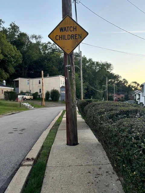 A pole with a "watch children" sign blocks the sidewalk completely