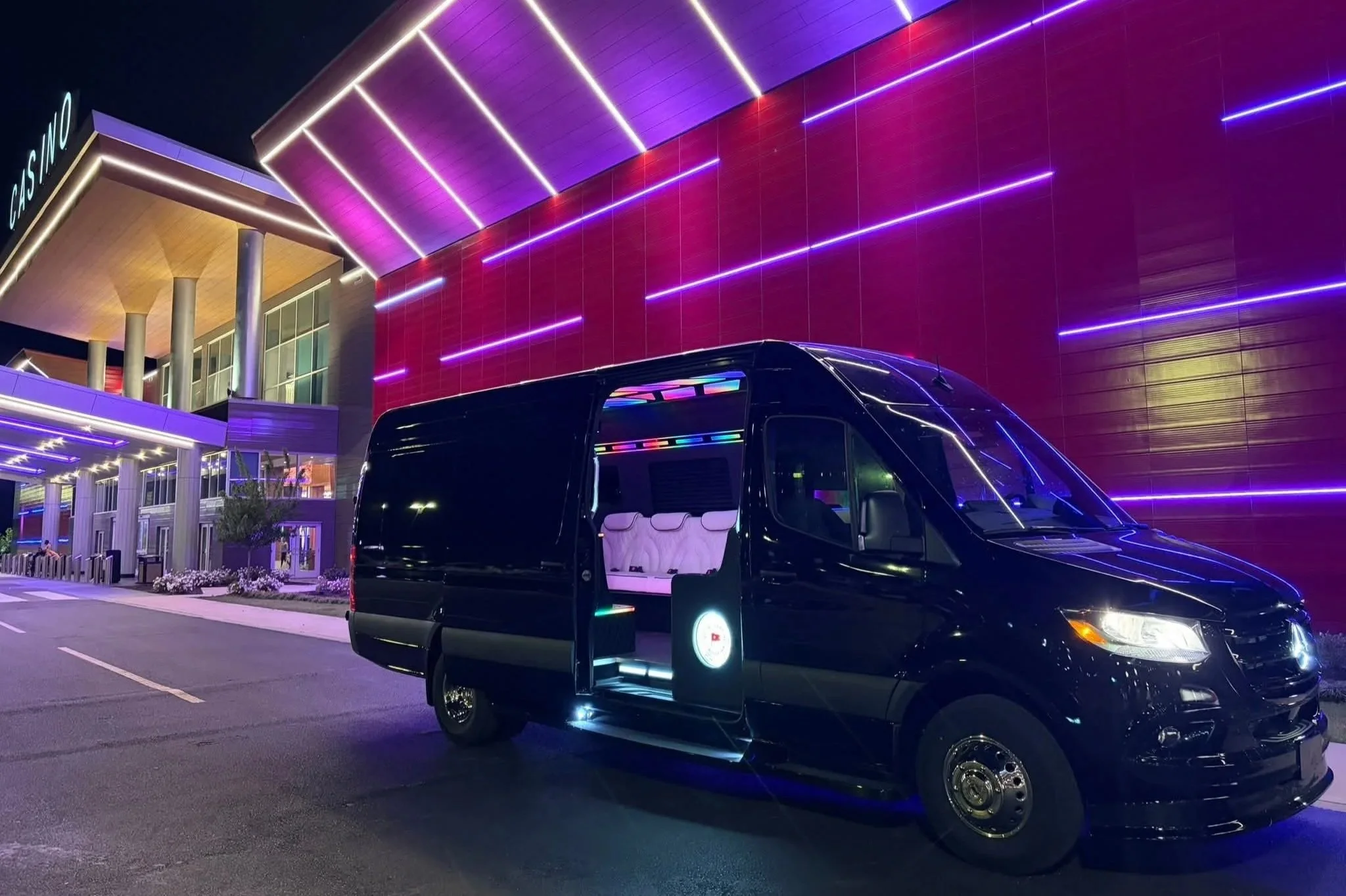 Nighttime scene of a modern building with colorful LED lights on the exterior and a black limousine with interior lighting parked outside.