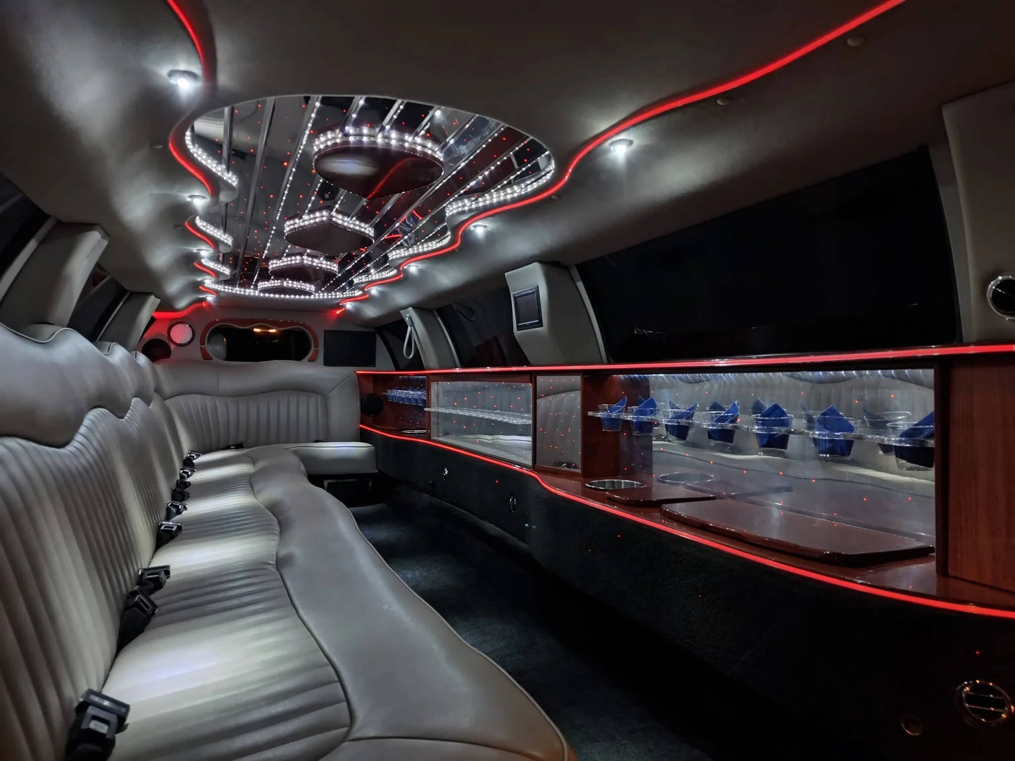 Luxury limousine interior with beige leather seating, red LED accent lighting, and a mirrored ceiling with LED lights.