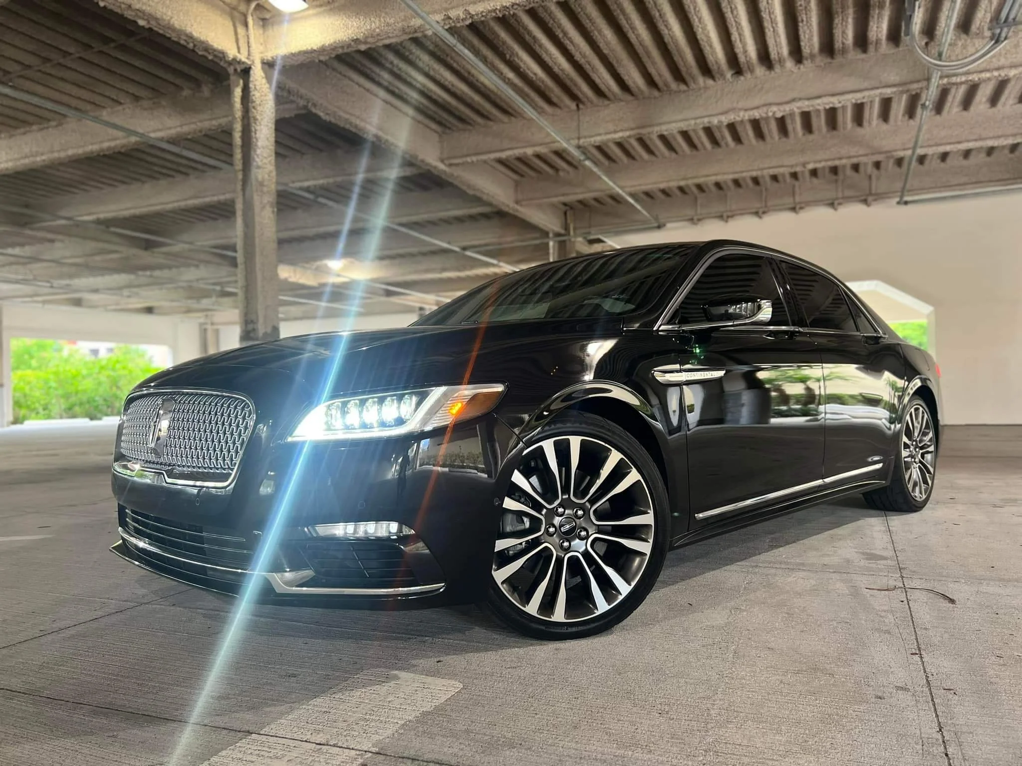 Black luxury sedan parked in an indoor parking garage with bright headlights