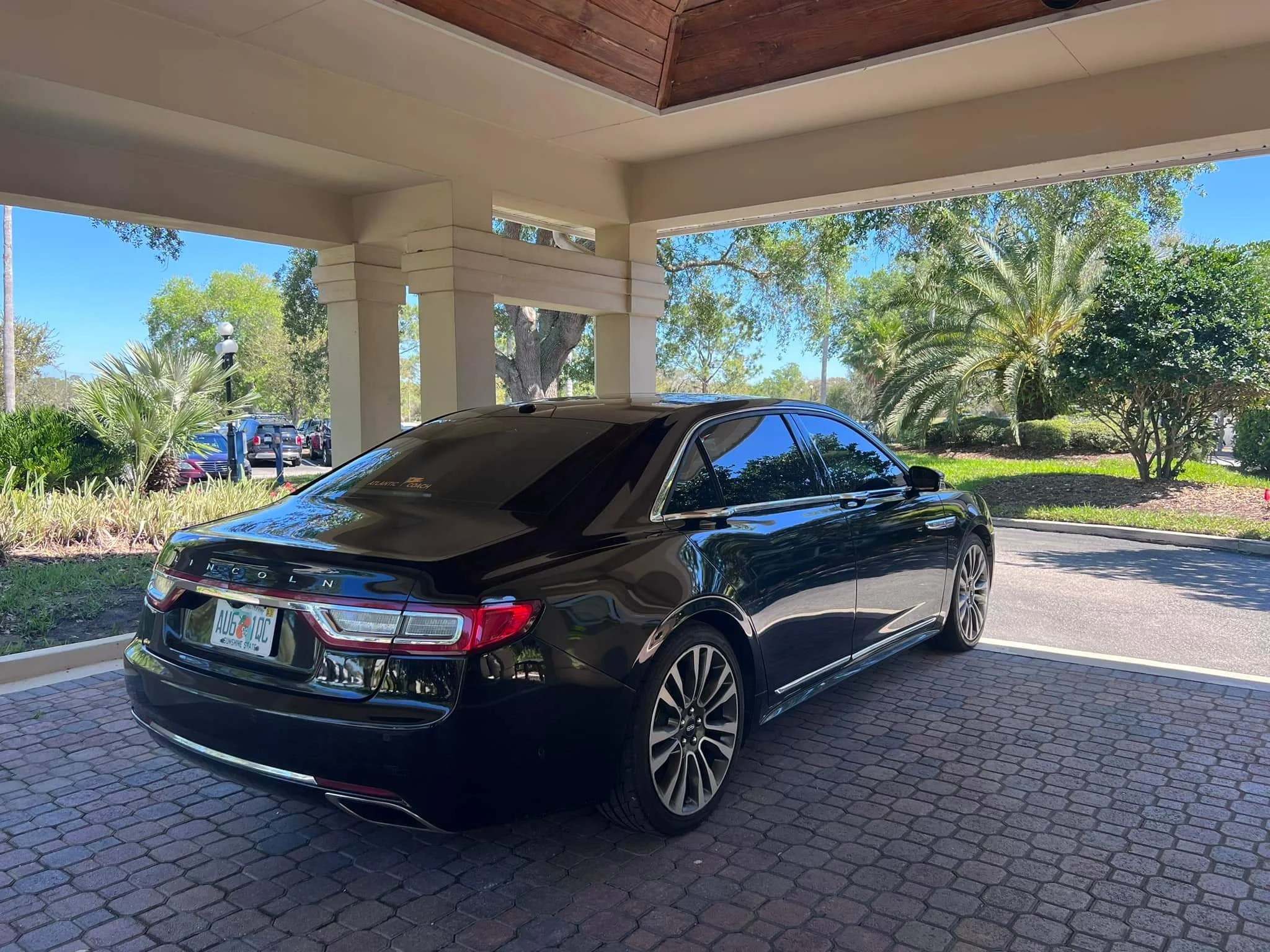 Black Lincoln sedan parked under a covered area with palm trees and greenery in the background.