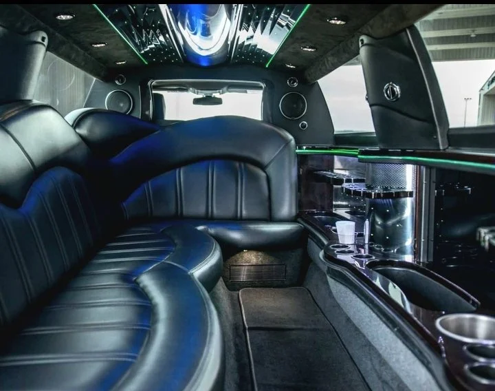 Interior of a luxury limousine with black leather seating, chrome accents, and LED lighting.