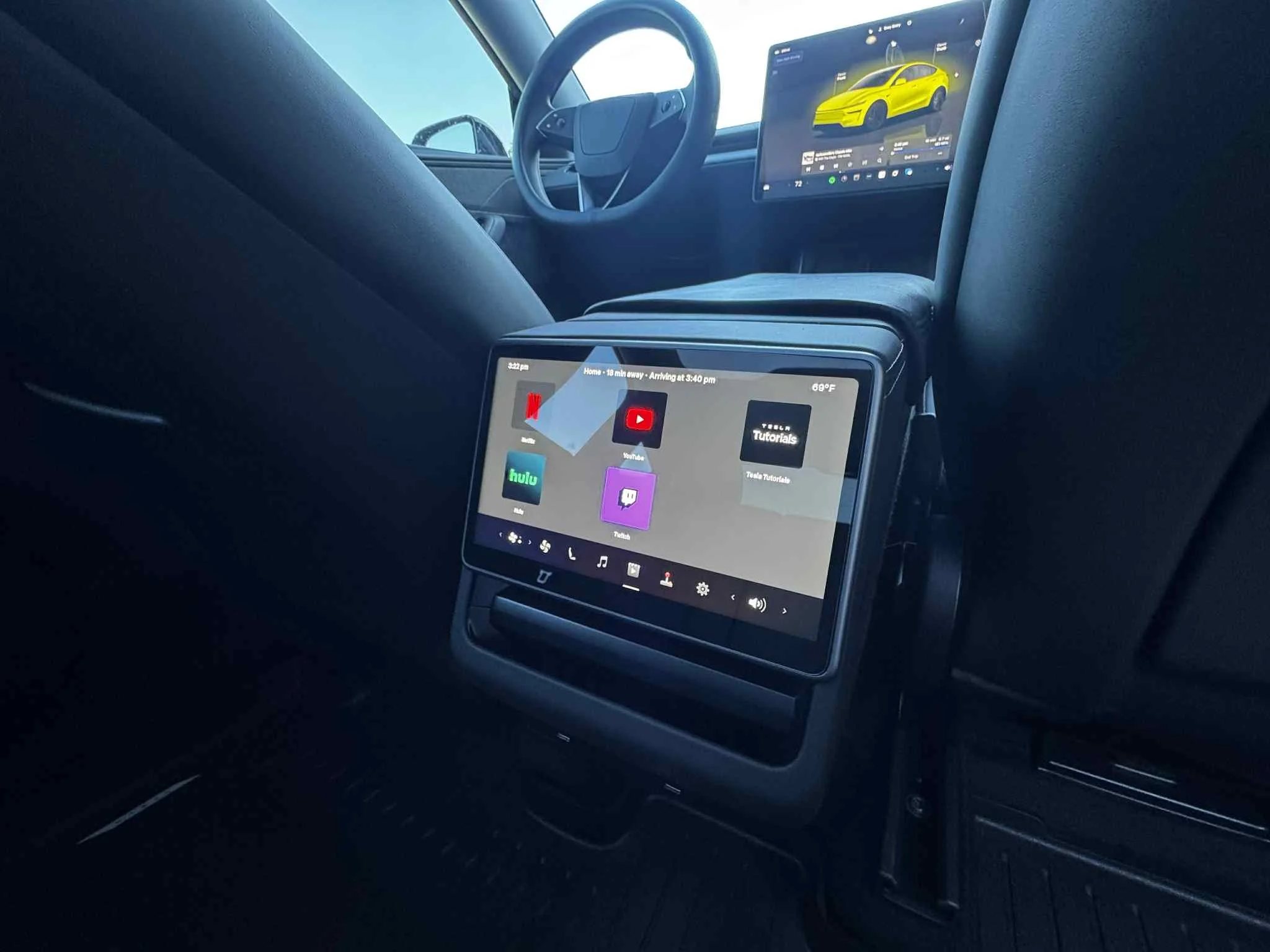 Backseat view of a vehicle with two digital screens, one mounted on the back of the front seat showing streaming app icons, and the other on the dashboard displaying a car illustration.