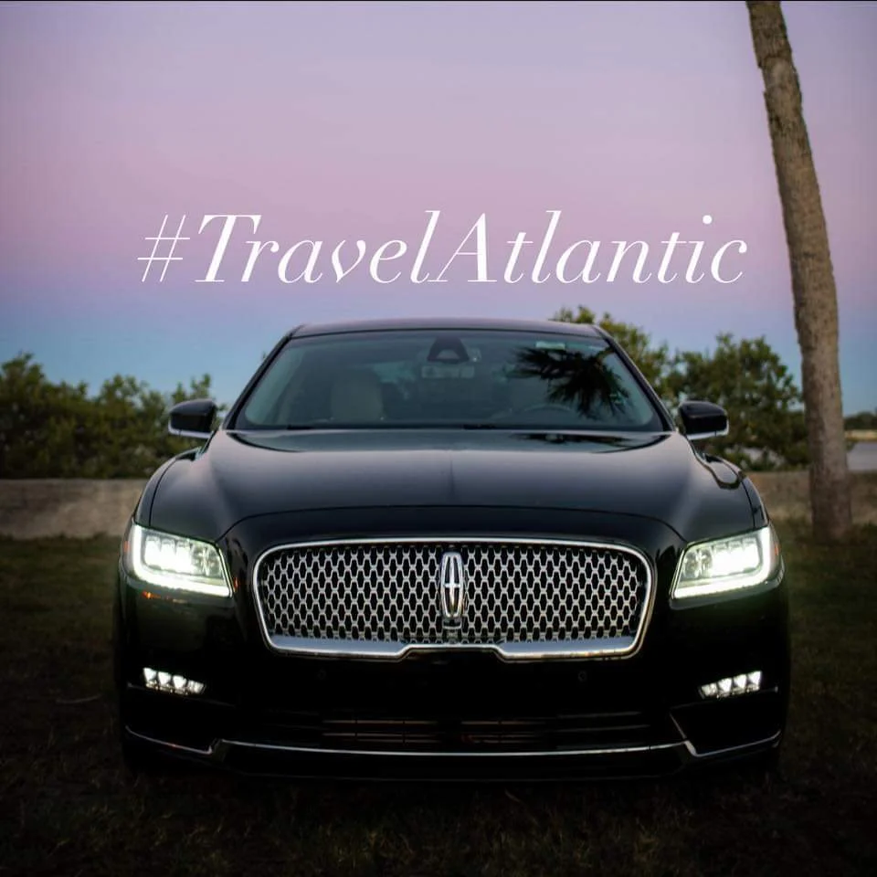 Black luxury car with illuminated headlights parked outdoors during dusk, with 