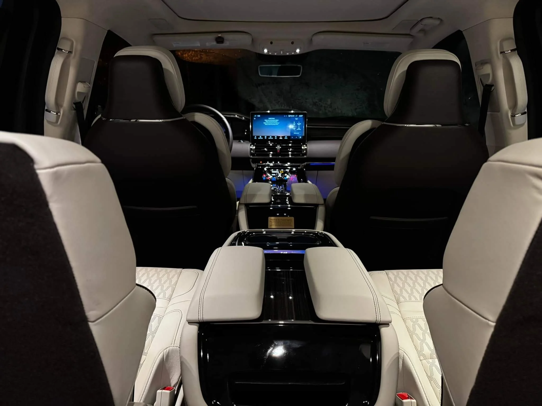 Inside an luxurious car with black and white leather seats, a digital dashboard, and ambient lighting.