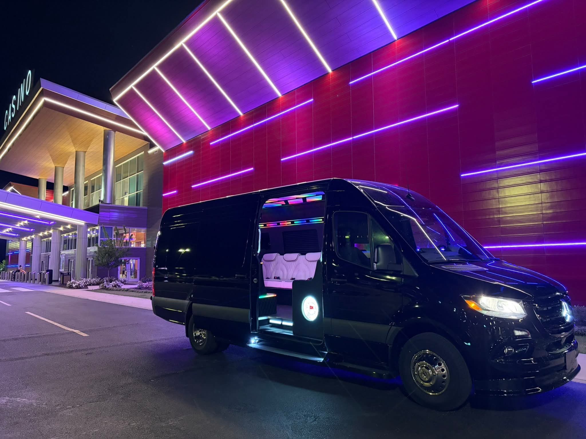 Nighttime scene of a modern building with colorful LED lights on the exterior, with a black limousine parked in front.