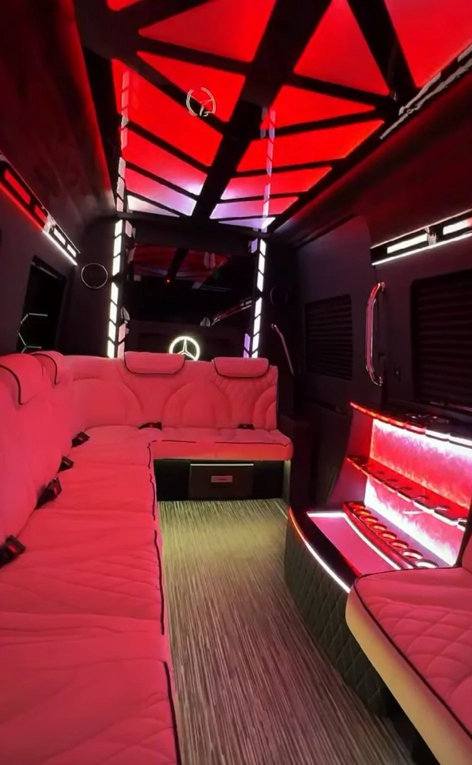 Inside a limousine with red velvet seating, black and red interior decor, LED lighting, and a Mercedes-Benz logo illuminated on the wall.