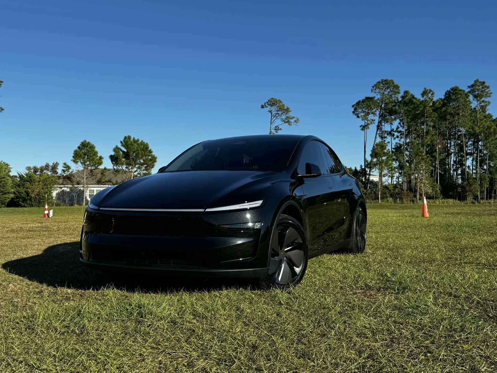 A black electric car parked on a grassy field with a blue sky and trees in the background.