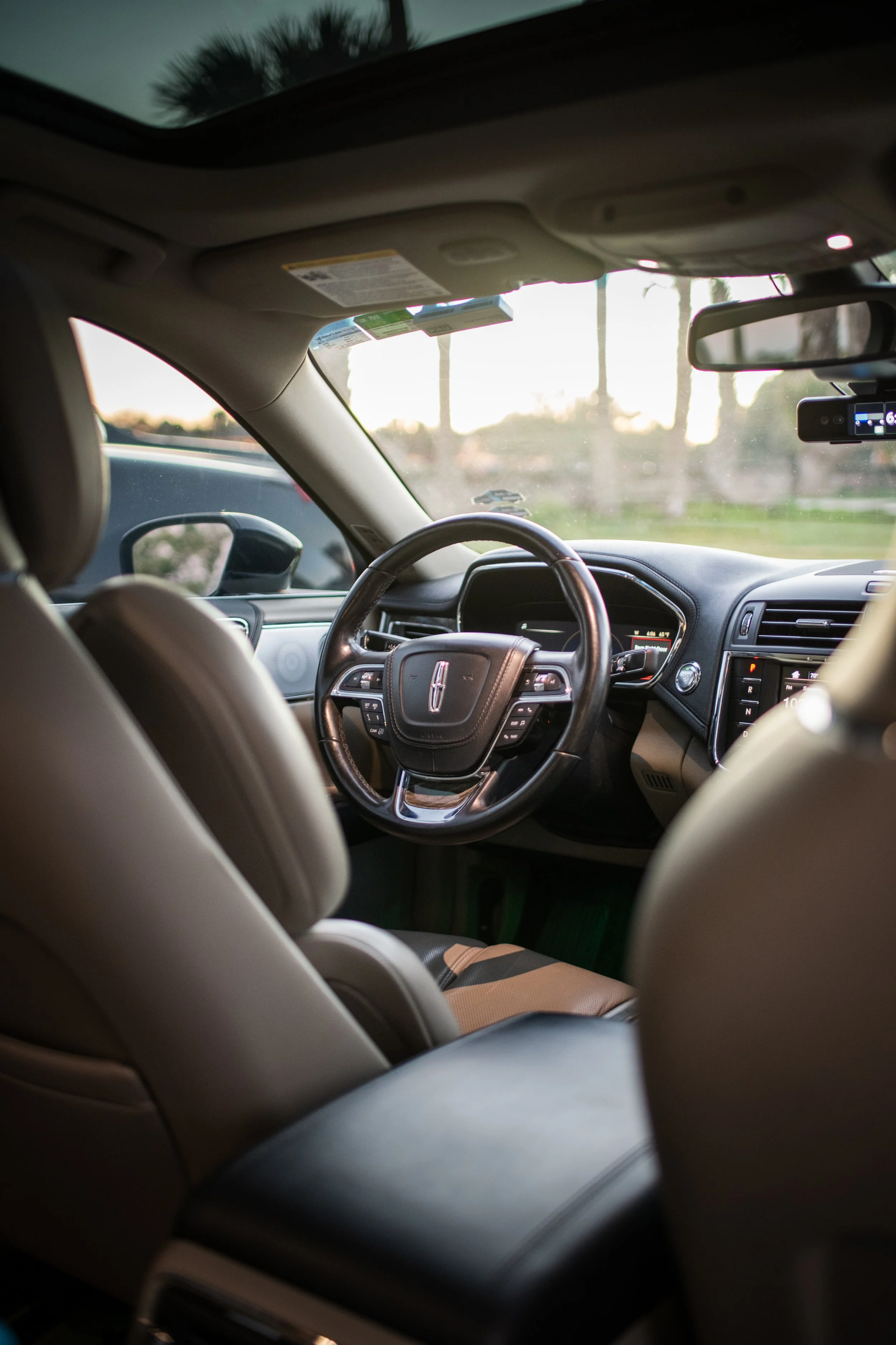 Interior of a car from the back seat, showing the steering wheel and dashboard with sunlight outside the car window.