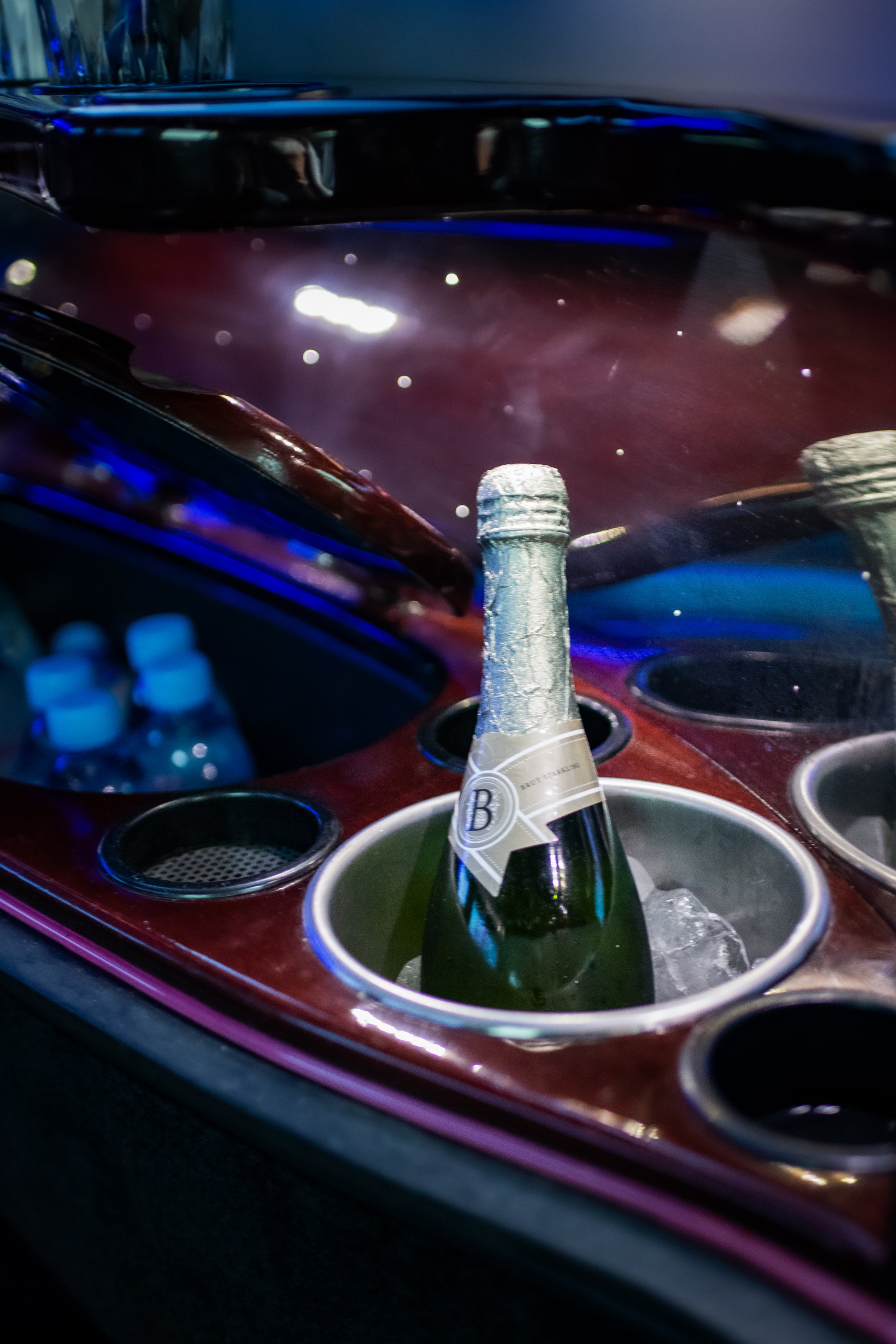 A bottle of sparkling wine in a wine cooler filled with ice, situated in a car's dashboard cup holder.