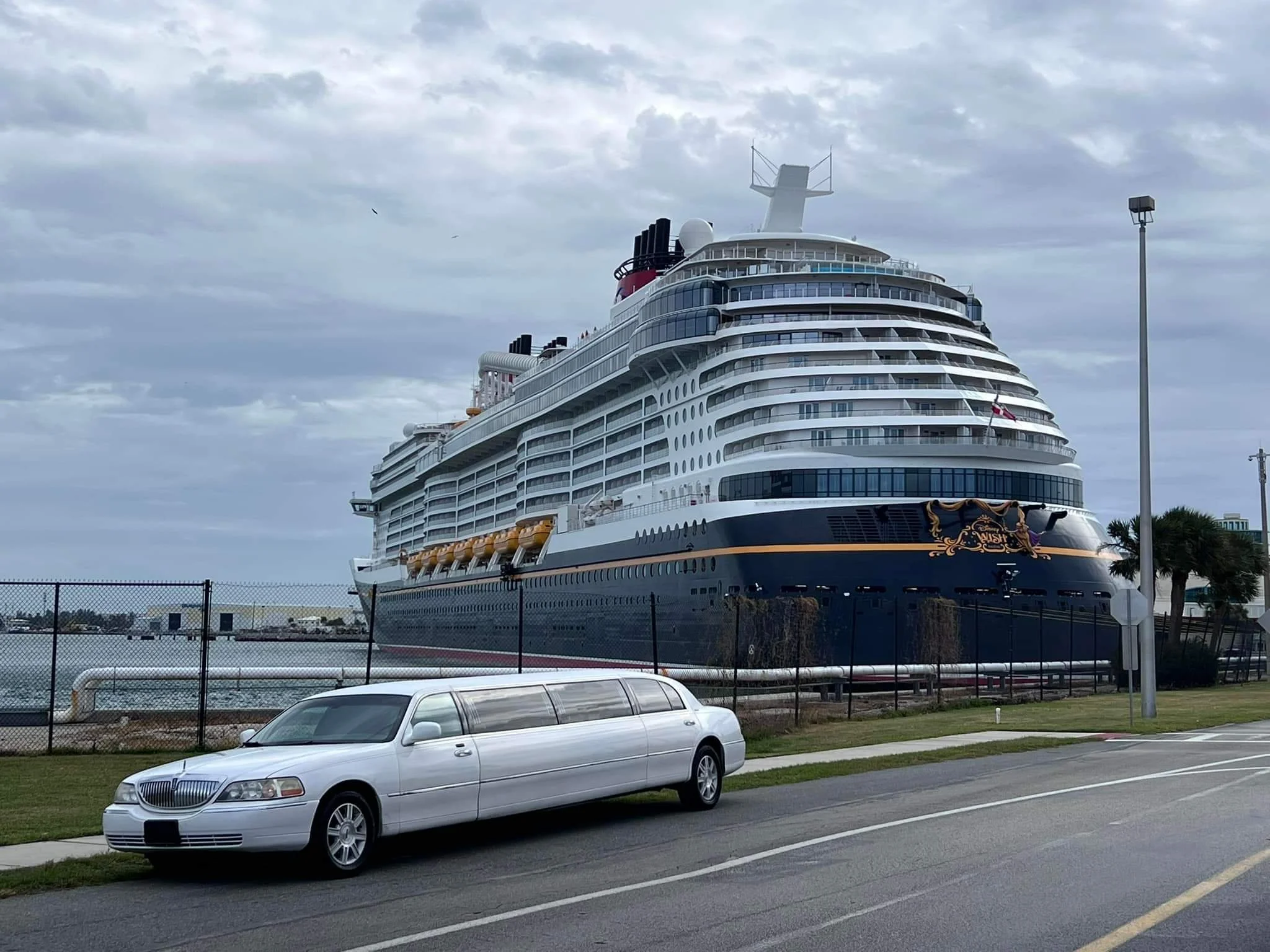 Large cruise ship docked at port with a white limousine parked in front.