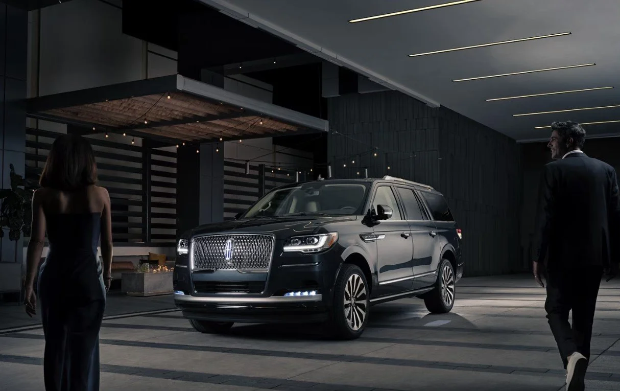 A black luxury SUV in a modern showroom with two well-dressed people, a woman and a man, nearby.
