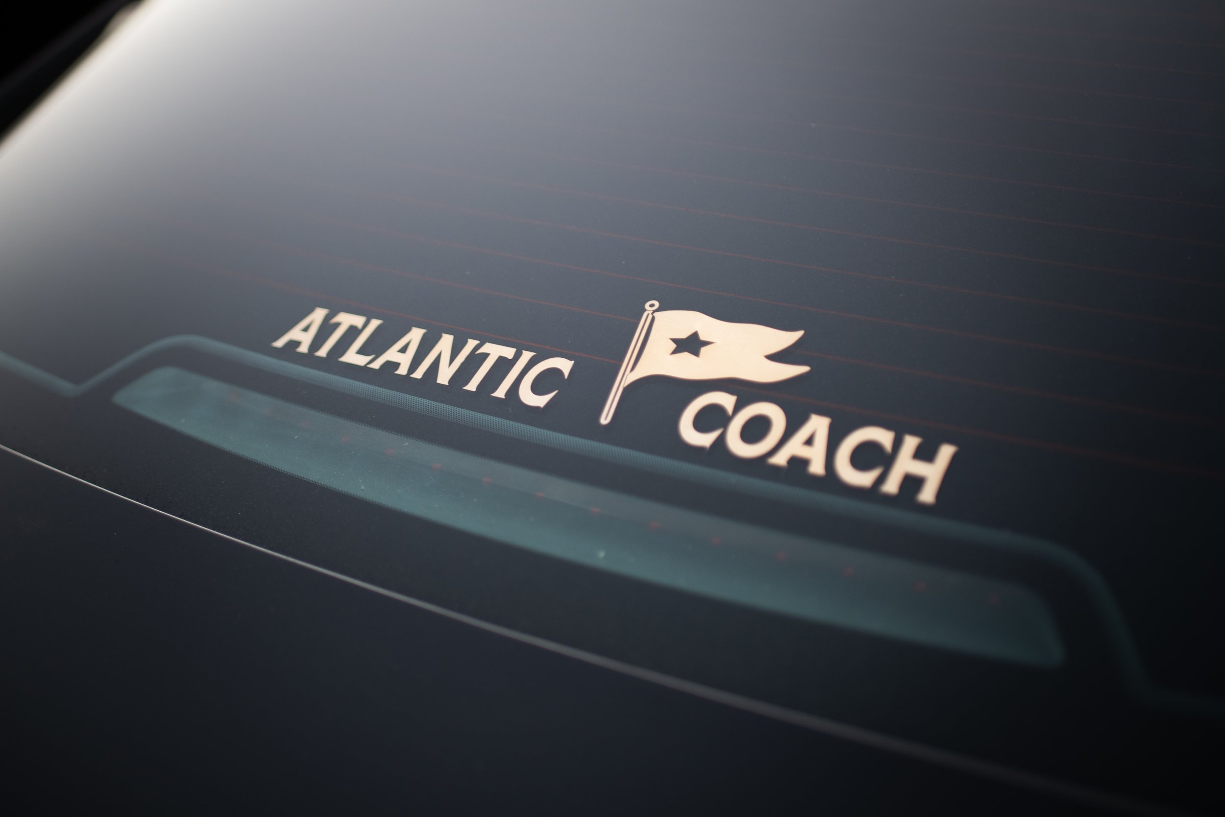 Close-up of a car rear window with white decal reading 'Atlantic Coach' and a small flag with a star on it.