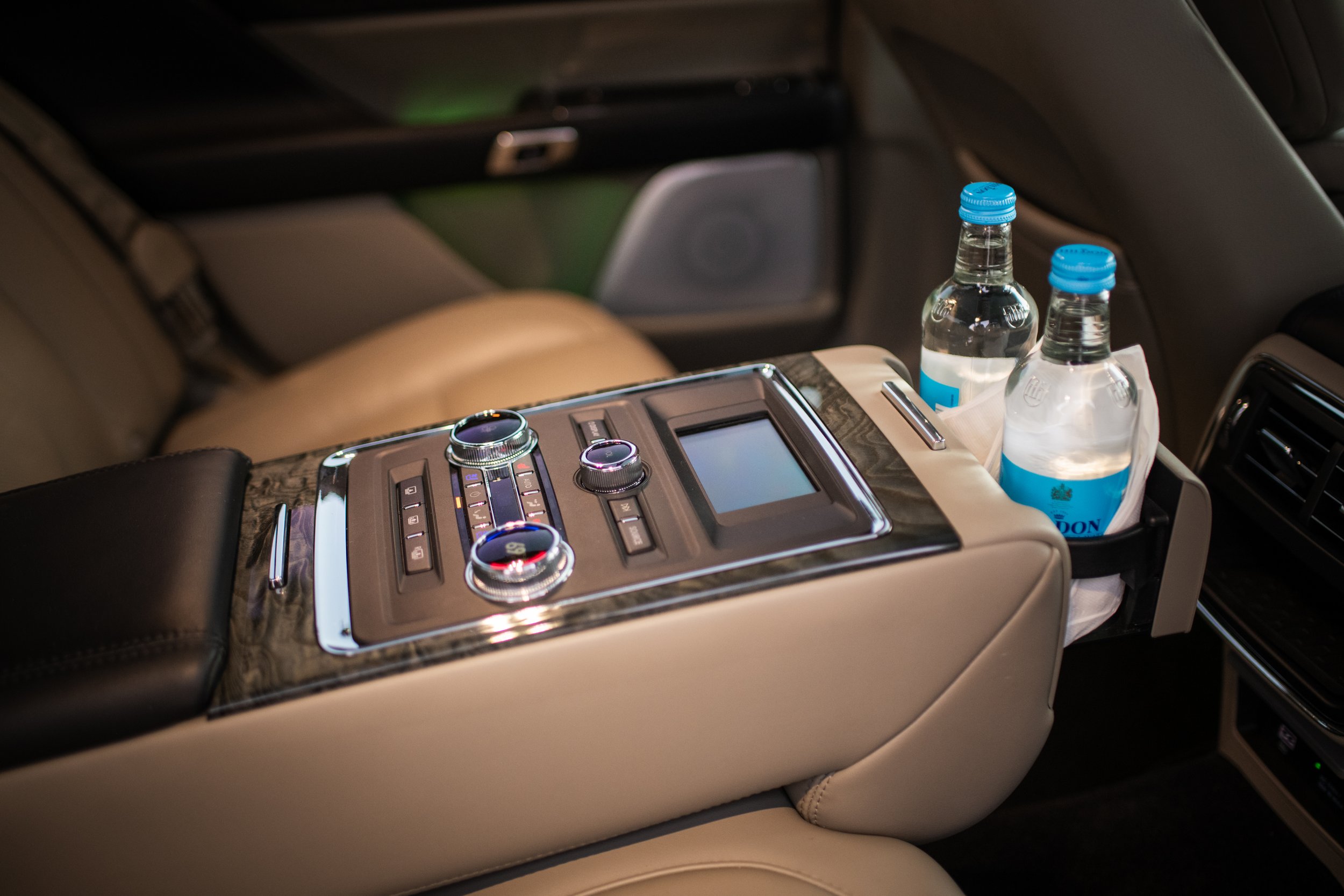 Luxury car interior with control panel, two water bottles in a side pocket, and leather seats.