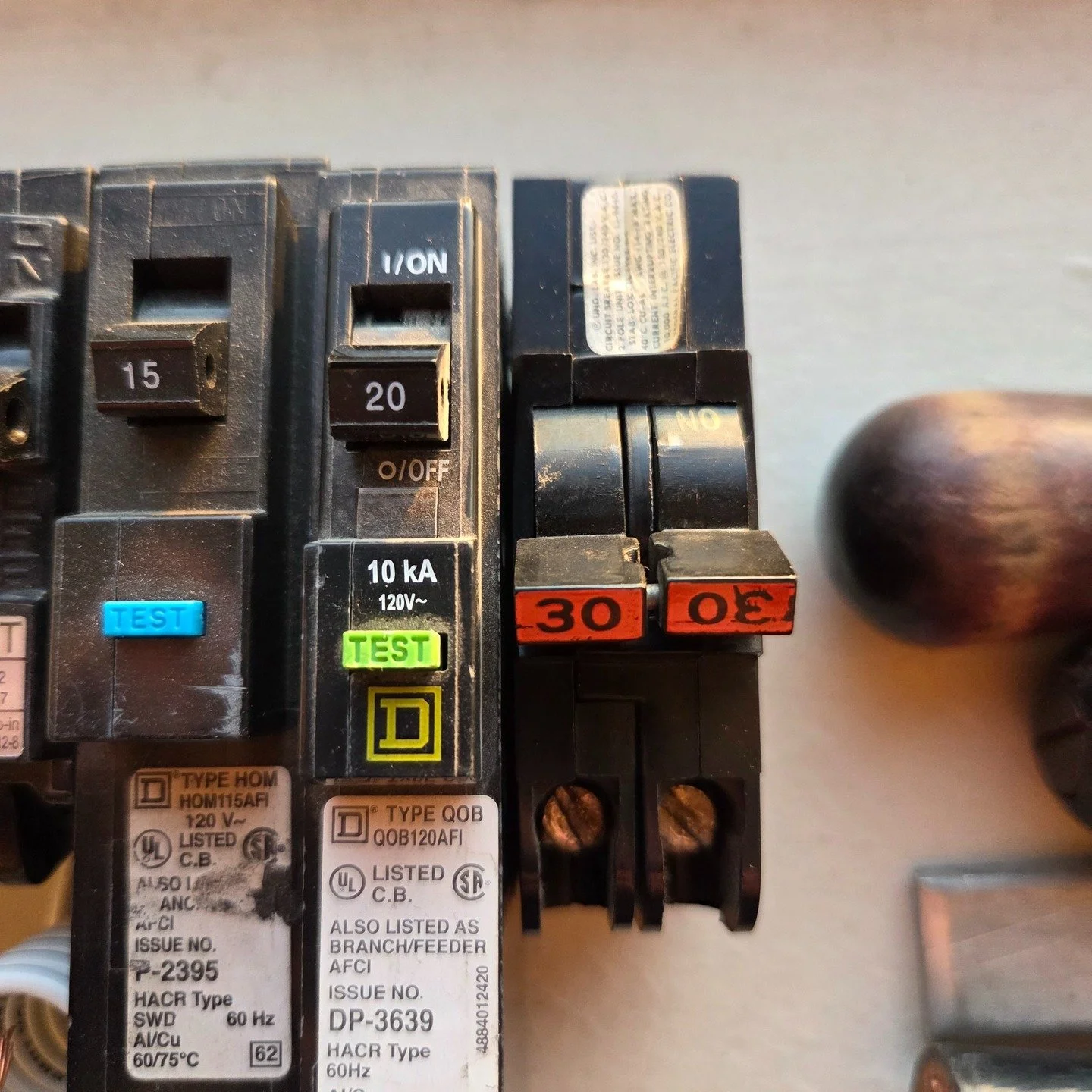In this picture a few obsolete or recalled circuit breakers can be seen. The breakers with the blue and lime buttons are older models of AFCIs which have been recalled. The orange-handled breaker is a Federal Pacific brand breaker; known for not alwa