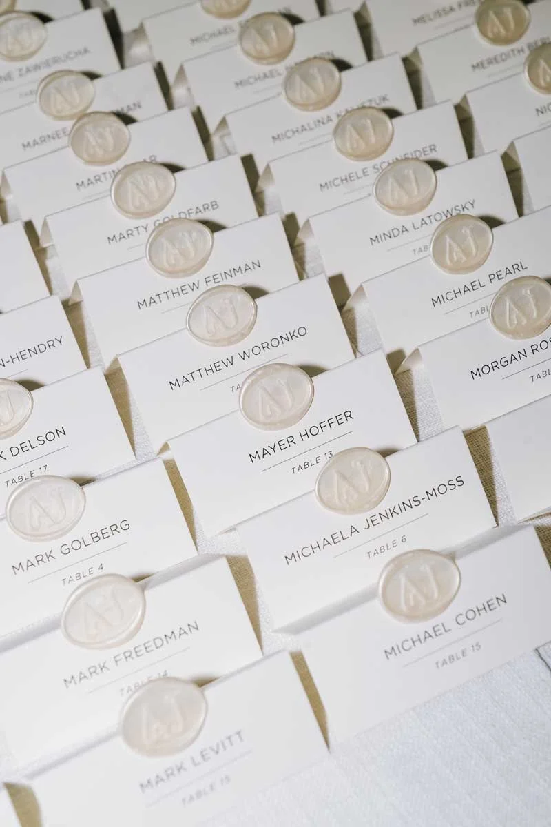 Table cards for a wedding reception with guests' names, table numbers, and wax seals featuring the letter 'N'.