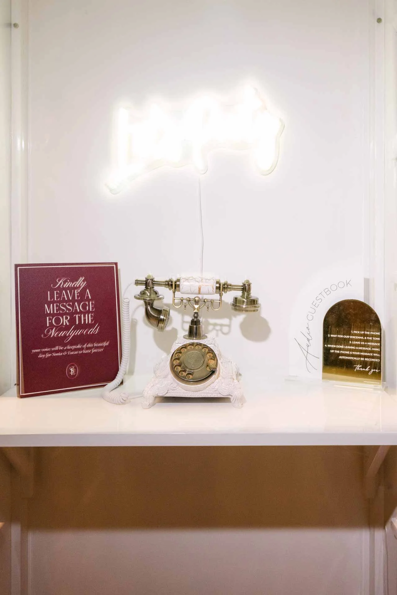 Vintage rotary phone with a white ornate base, displayed on a white shelf, flanked by informational signs about guestbook and message instructions.