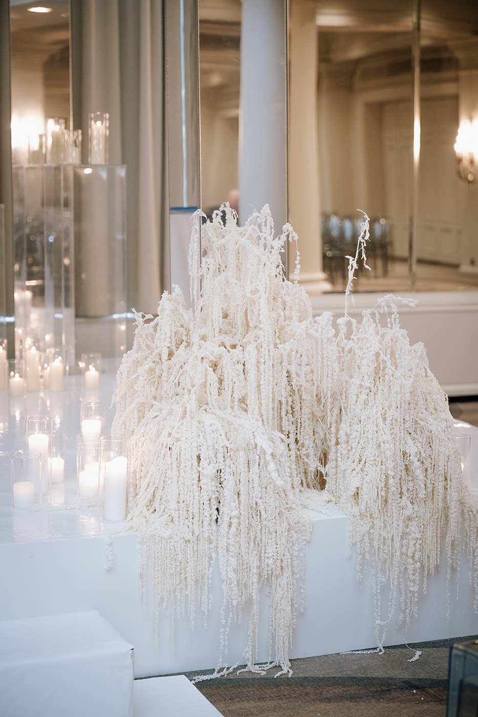 A white cascading floral arrangement with candles surrounding it, displayed on a table in an elegant, well-lit room.