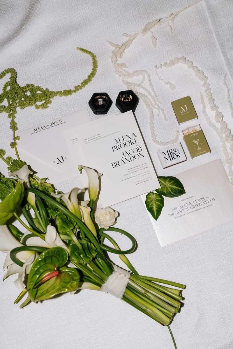 Wedding invitation with rings, flowers, and stationery on a white table.