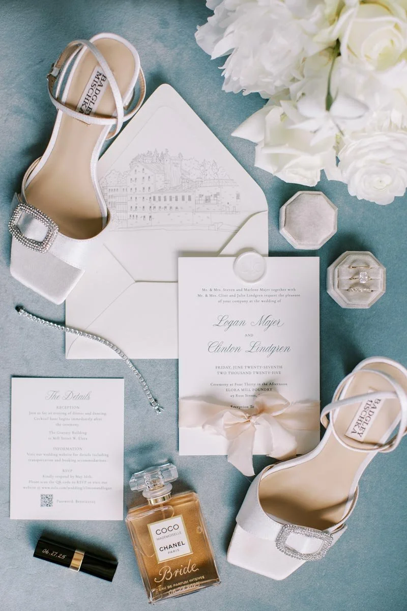 Wedding invitation, shoes, perfume, jewelry, and floral arrangement for a bride.
