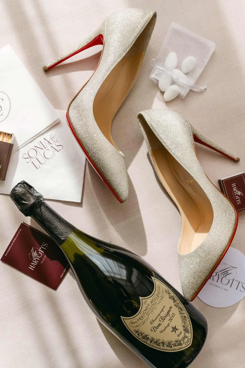A pair of high-heeled shoes with red soles, a bottle of champagne, and some candy in a small pouch, key card holder and custom napkins
