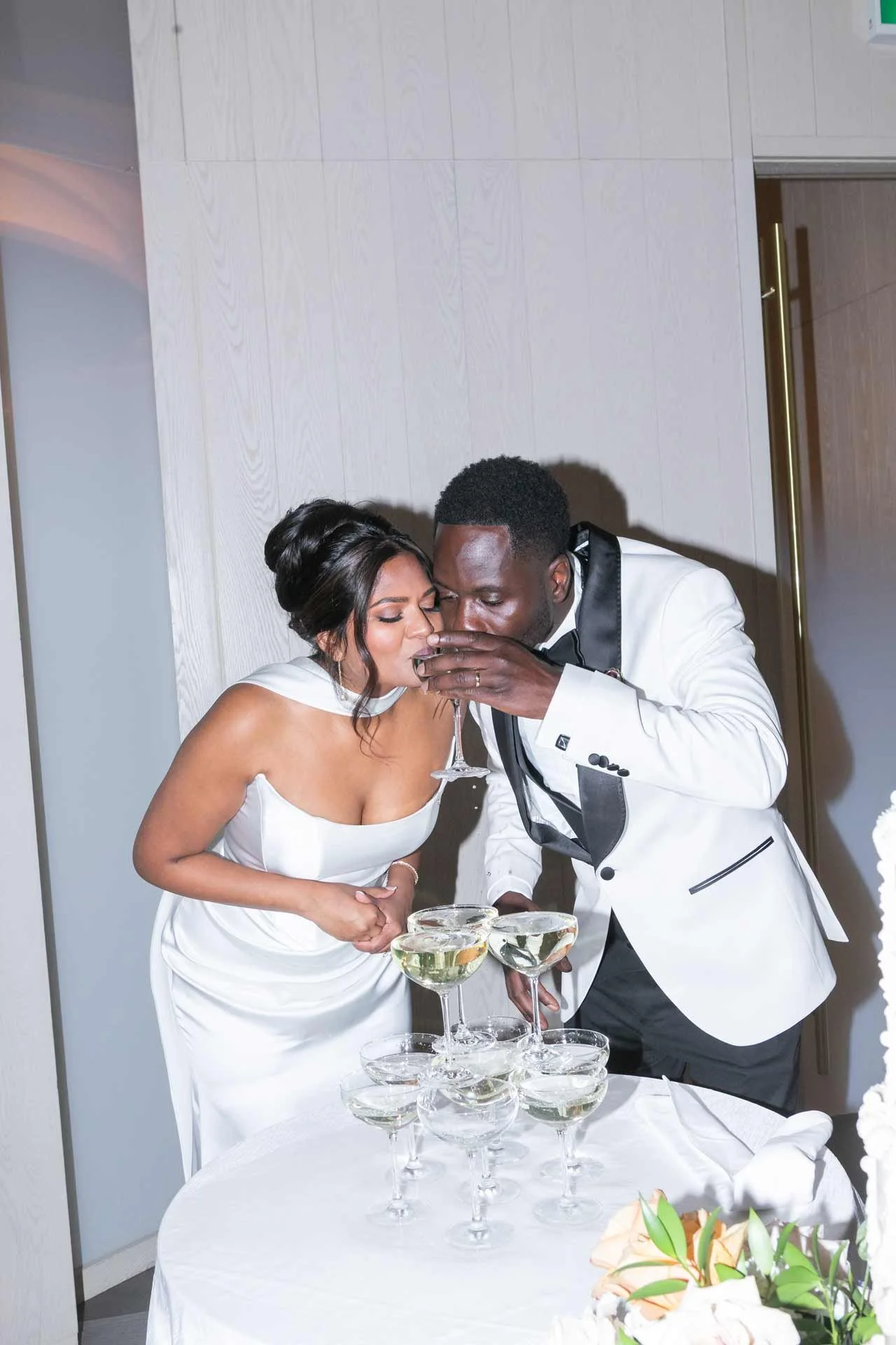 A newlywed couple in formal attire toasting with champagne glasses at their wedding reception.