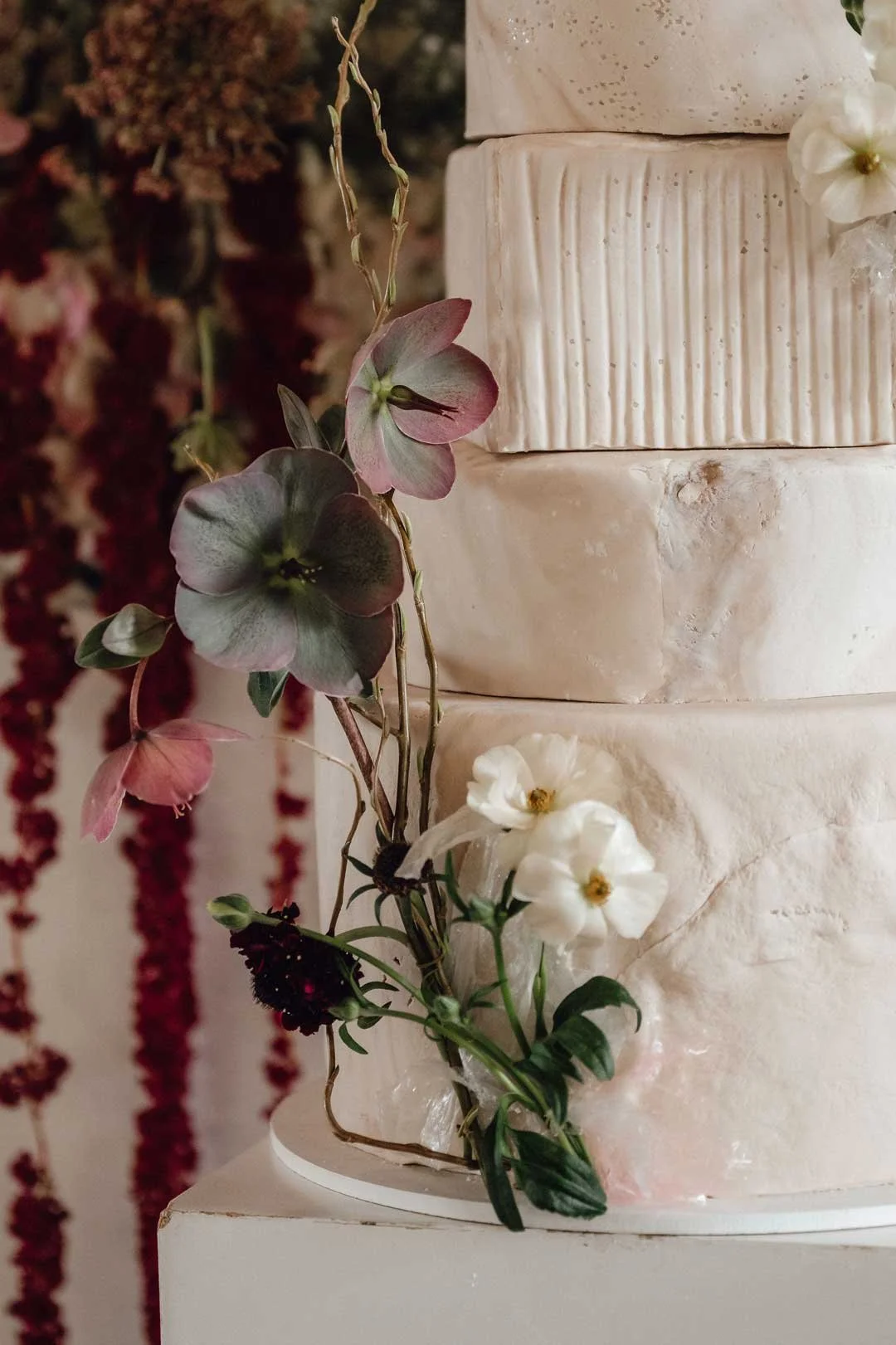 Close-up of a tiered wedding cake decorated with white and pink flowers and greenery.