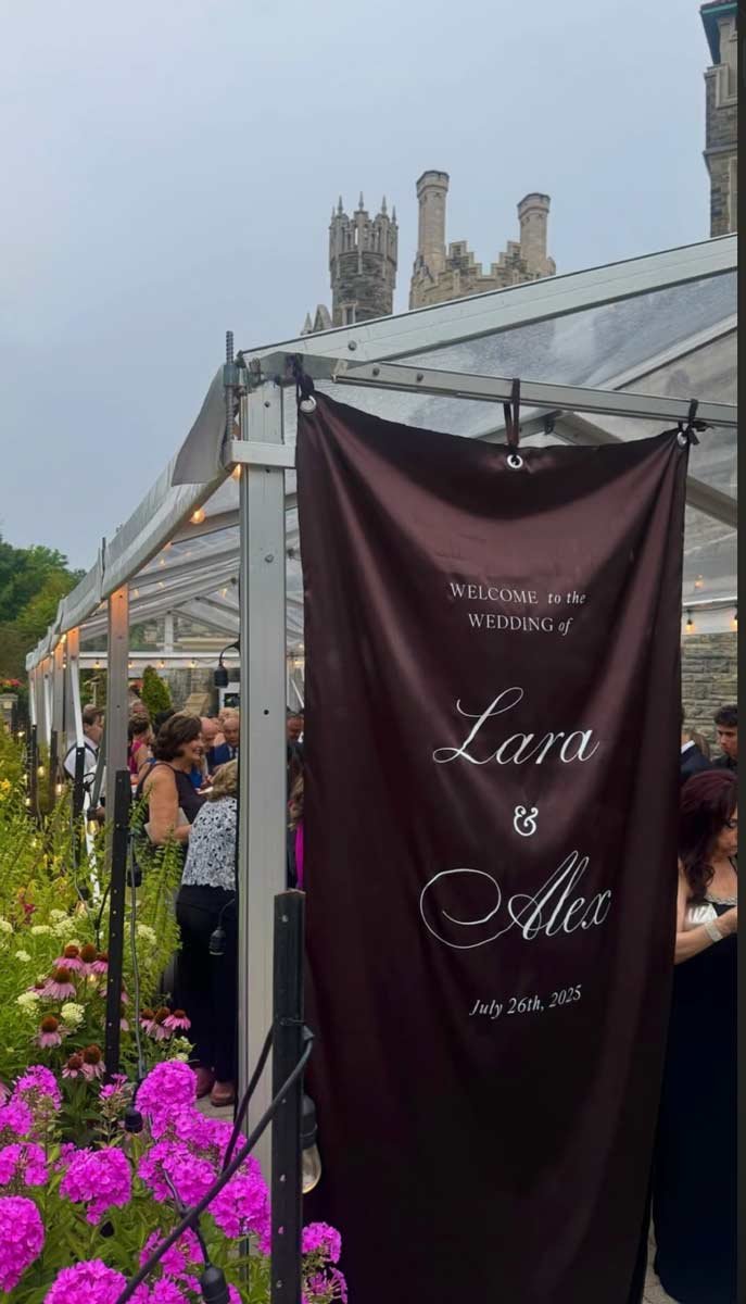 Wedding reception gathering outside under a clear tent with purple flowers along the aisle and a castle in the background, for Lara and Alex, July 26th, 2025.