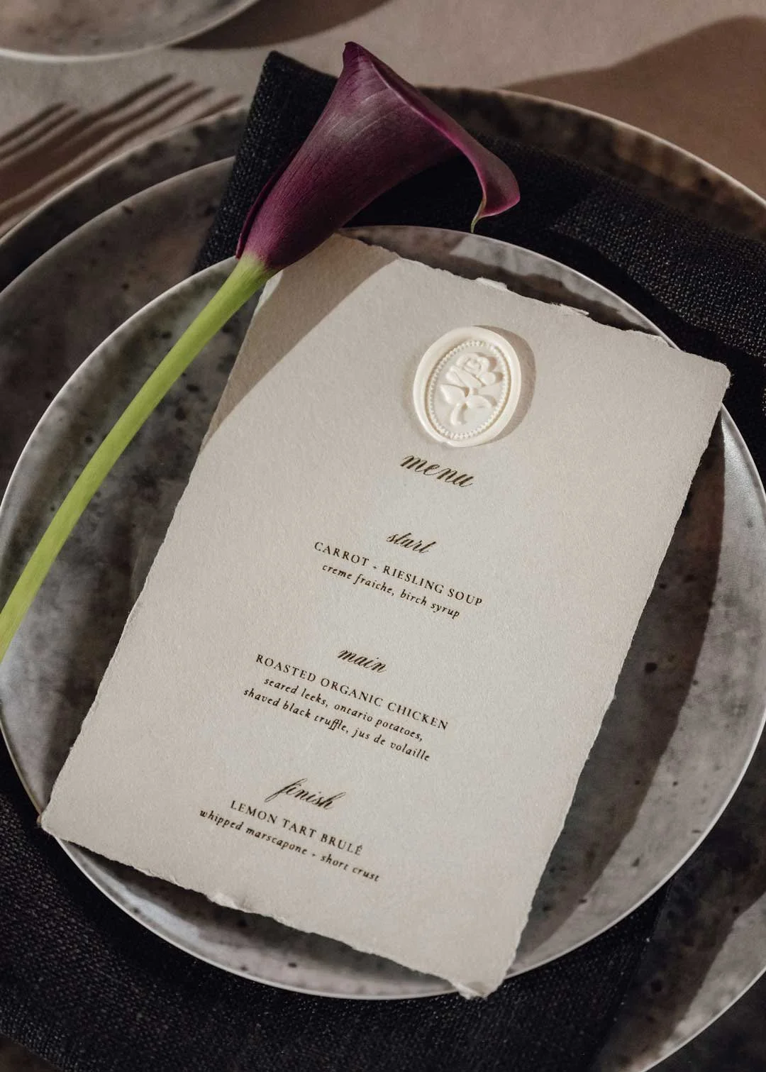 A elegantly designed restaurant menu with three courses listed: starter, main, and finish, topped with a purple calla lily flower on a plate.