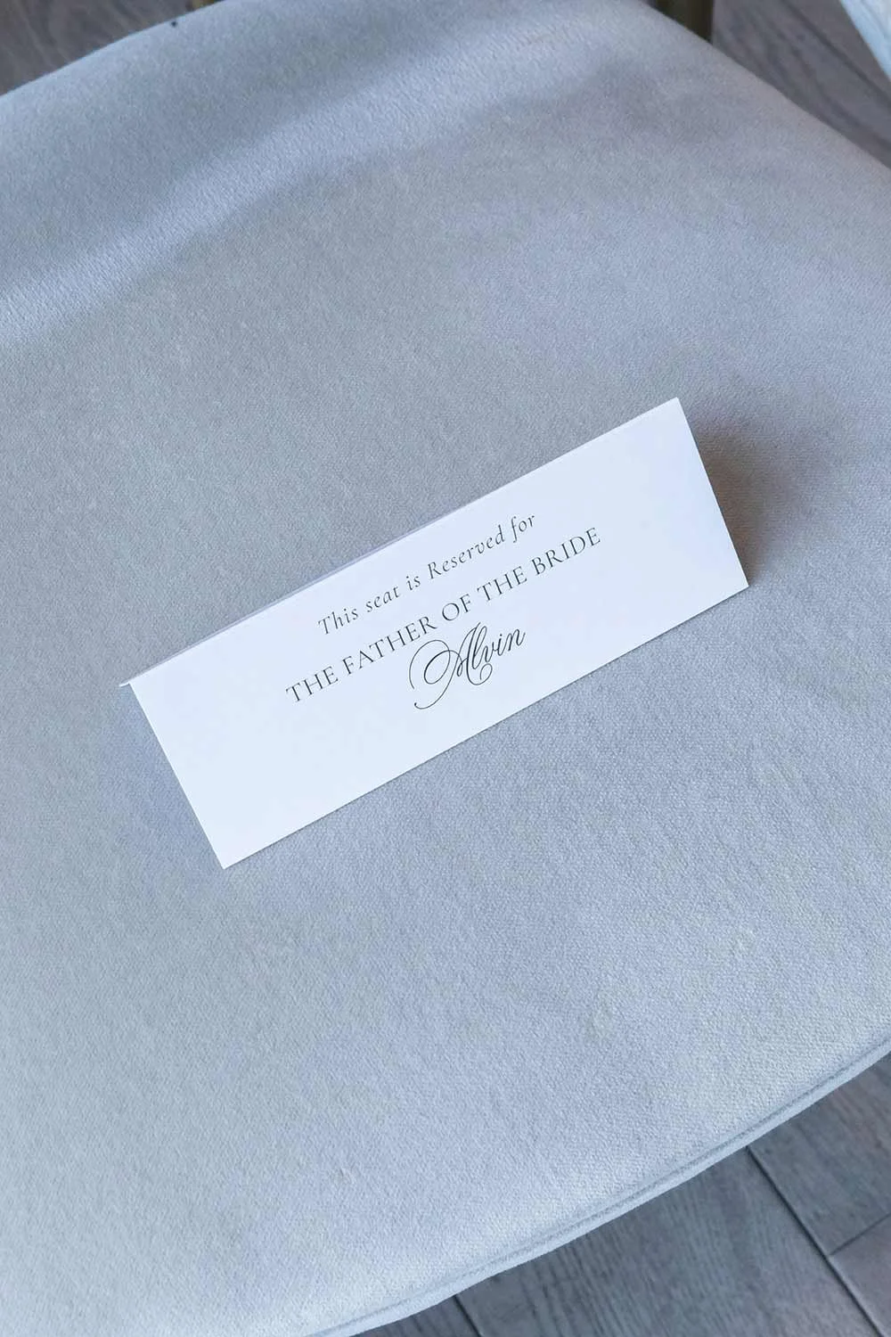 A reserved seat card on a light gray chair that reads 'This seat is Reserved for the Father of the Bride Alvin'.