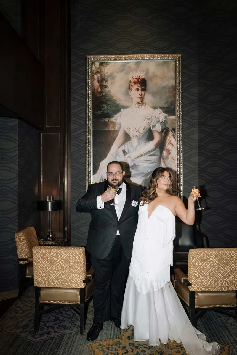 Bride and groom holding champagne glasses in front of artwork