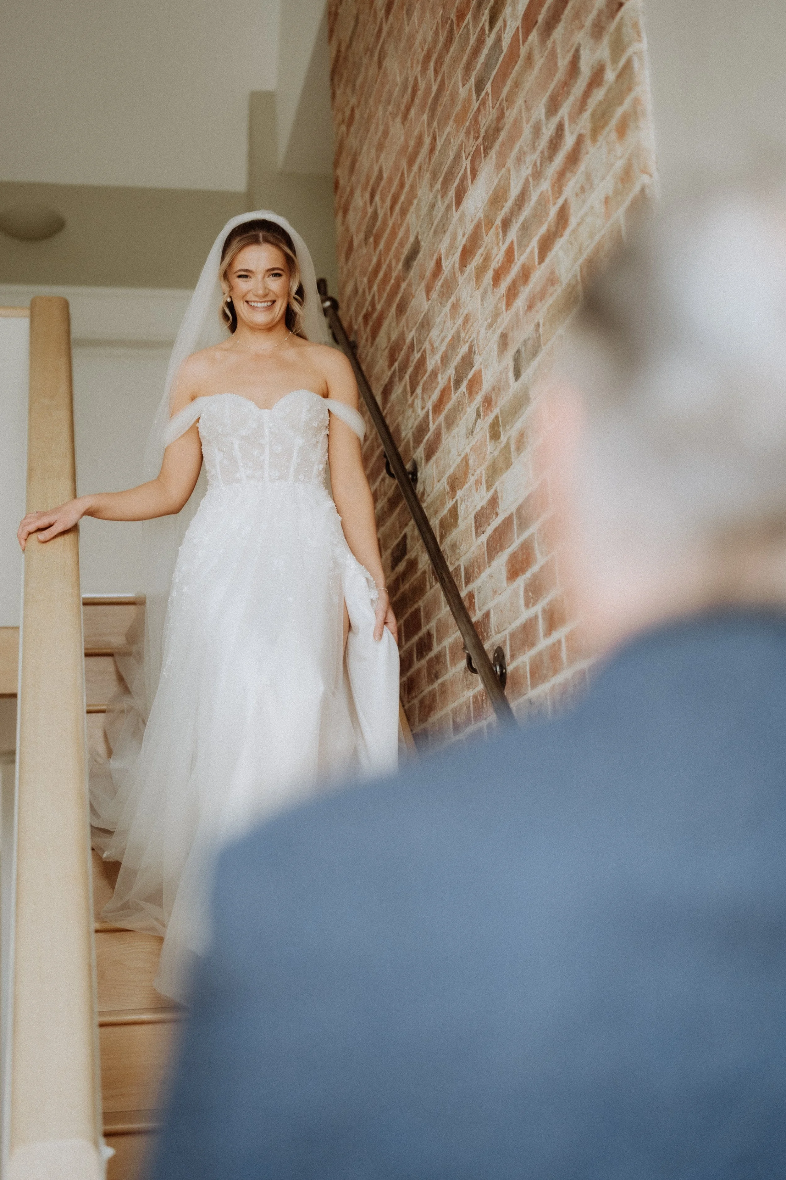 A bride to be in a wedding dress walking down the stairs smiling