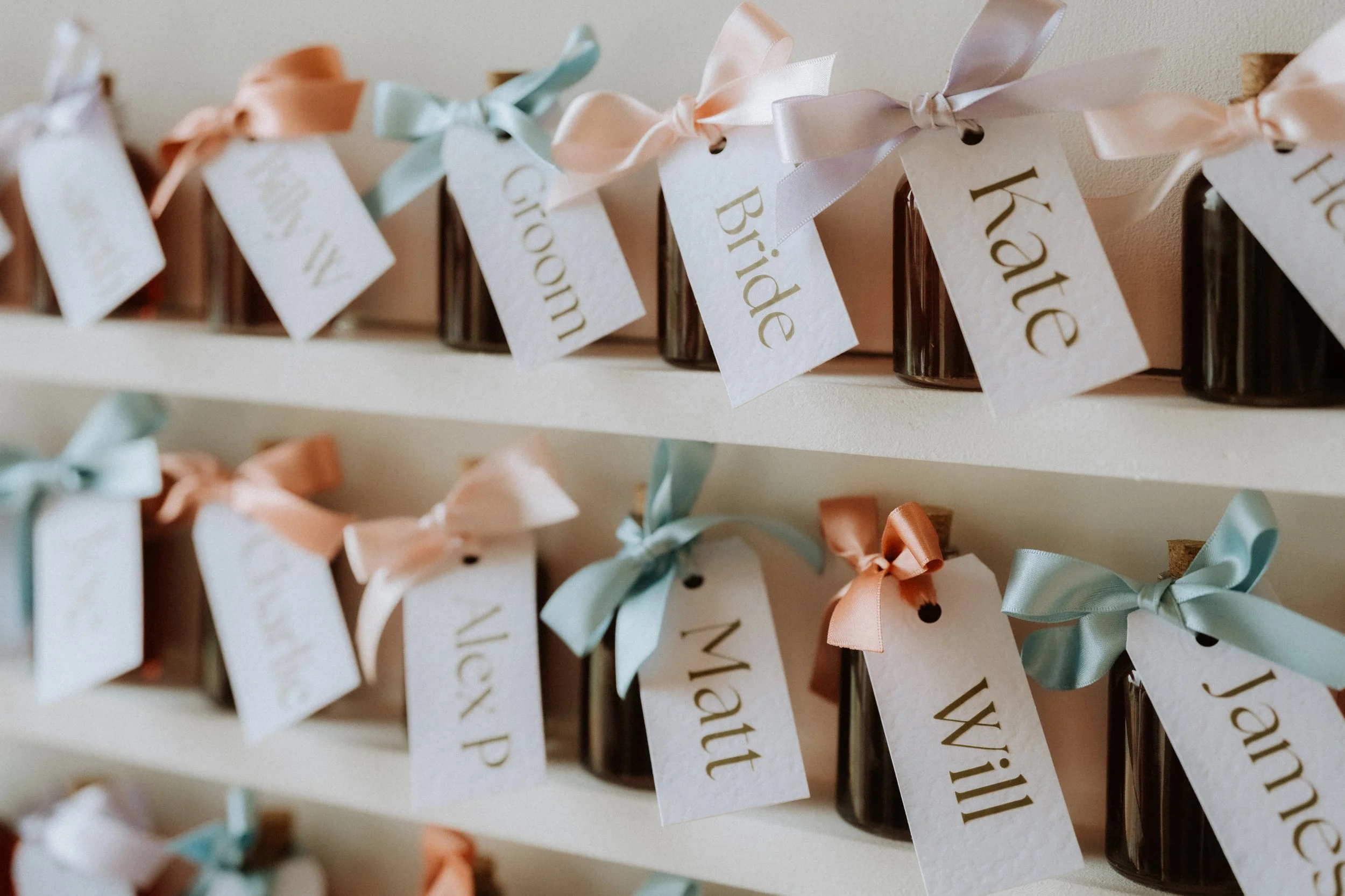 Small sloe gin jars with wedding guest names tied to them with colourful ribbons